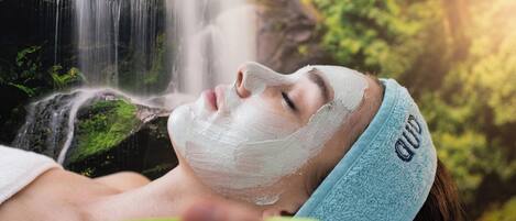 A person with a headband, lying down with a white substance on their face, in front of a waterfall.