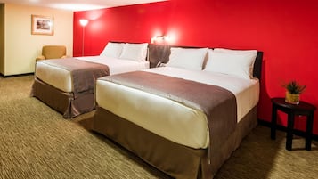A hotel room with two beds, a red accent wall, a small table with a plant, and a framed picture on the wall.