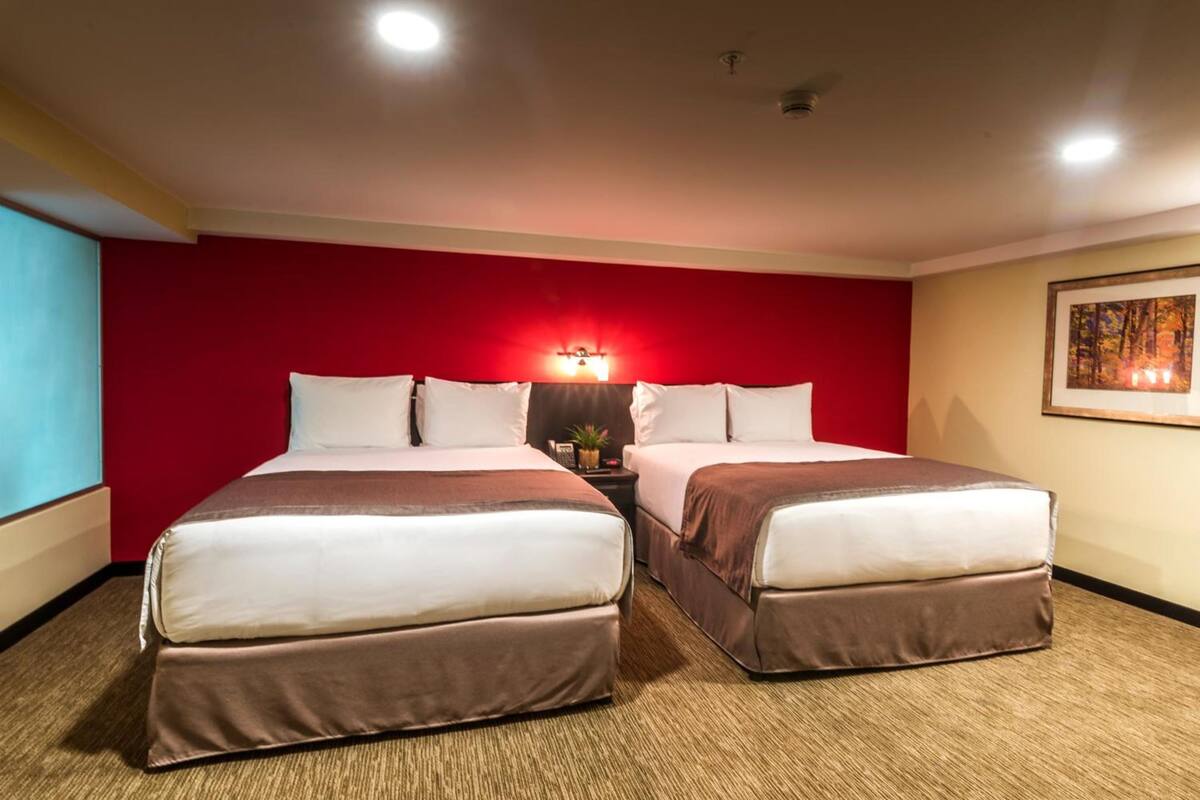 A hotel room with two beds, a red accent wall, a ceiling light, and a framed picture on the wall.
