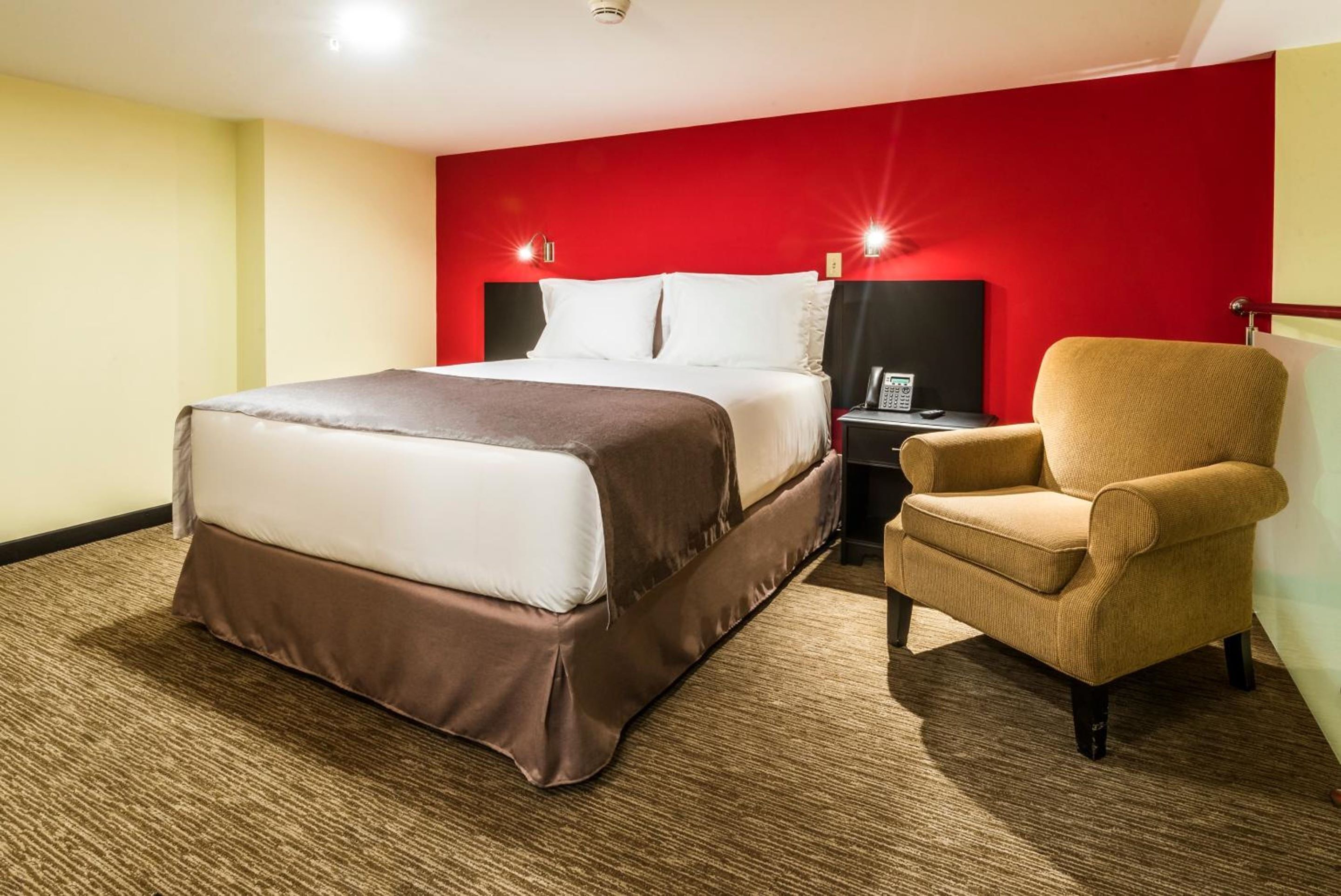 A hotel room with a bed, a nightstand, and a chair.
