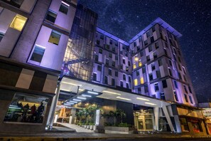 A multi-story hotel with a glass facade, a covered entrance, and a starry night sky.