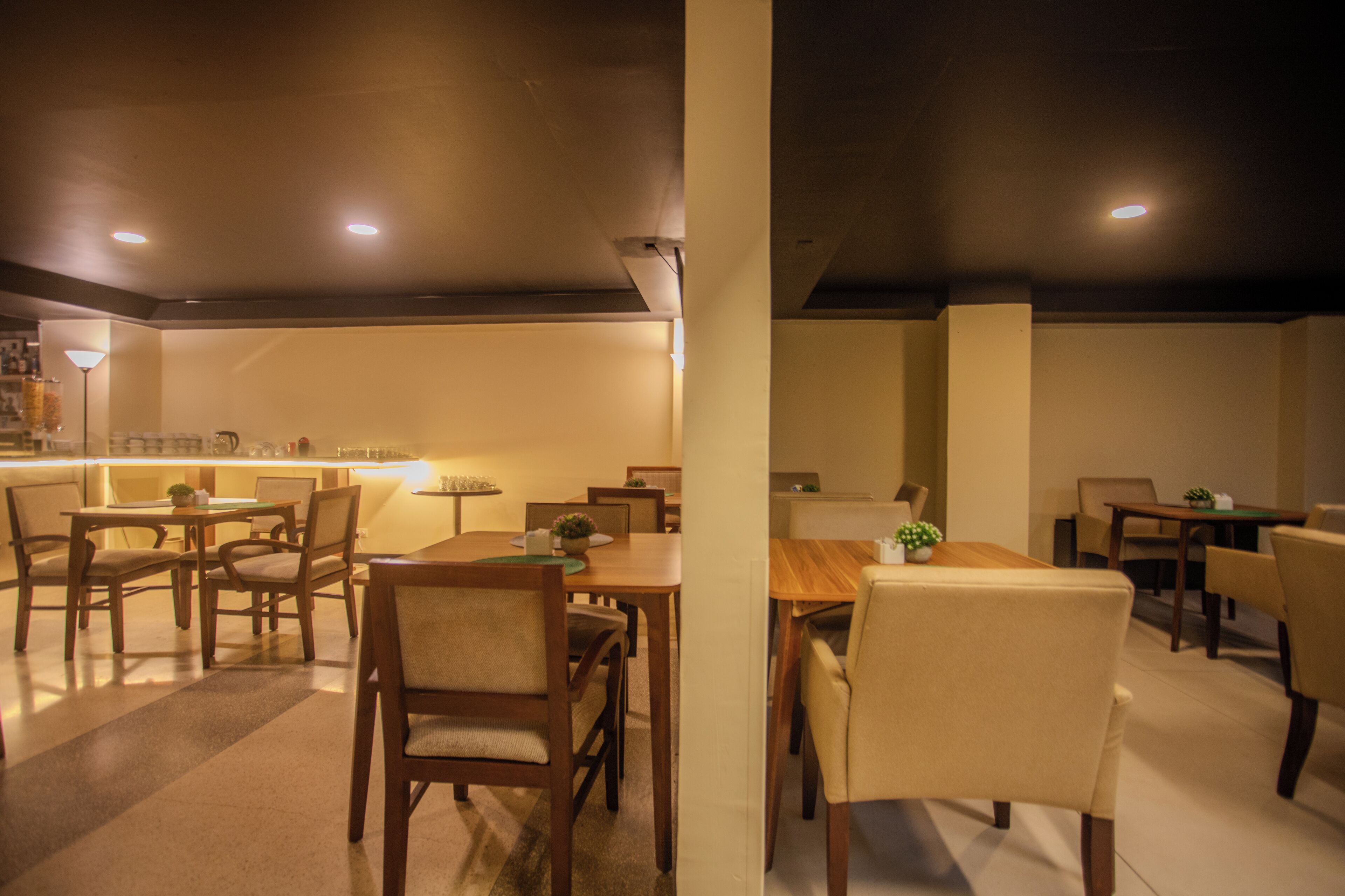 A dining area with multiple tables and chairs, a bar area with a counter and stools, and a ceiling with recessed lighting.