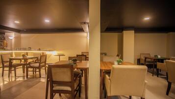 A dining area with multiple tables and chairs, a bar area with a counter and stools, and a ceiling with recessed lighting.