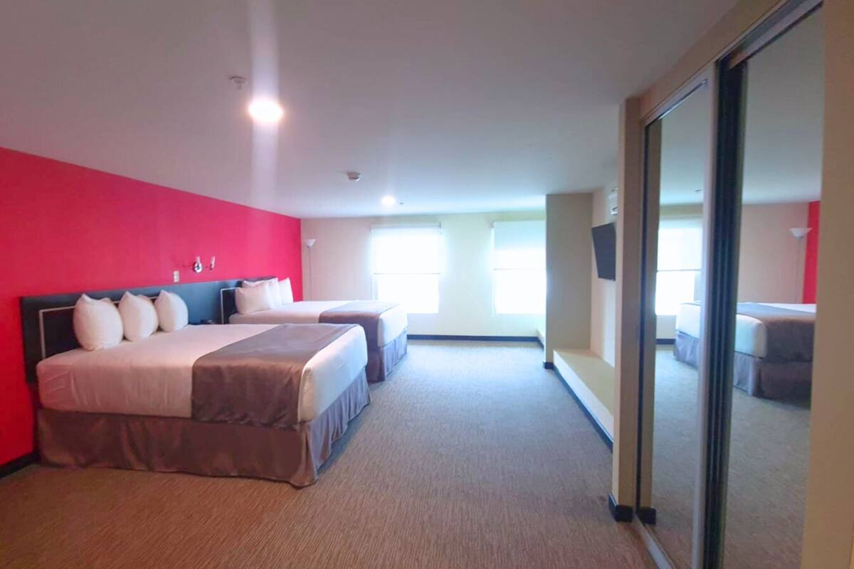 A hotel room with two beds, a red accent wall, and a sliding glass door leading to a balcony.