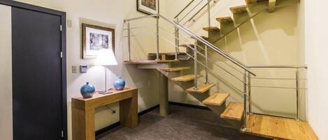 A staircase with wooden steps and metal railings, a wooden bench with vases, a door, and a framed picture on the wall.