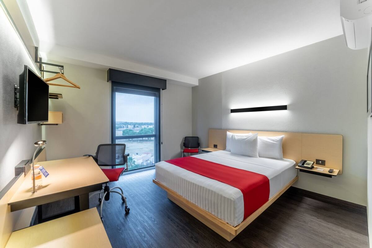 Una habitació d'hotel amb llit, escriptori, cadira i televisió penjada a la paret.