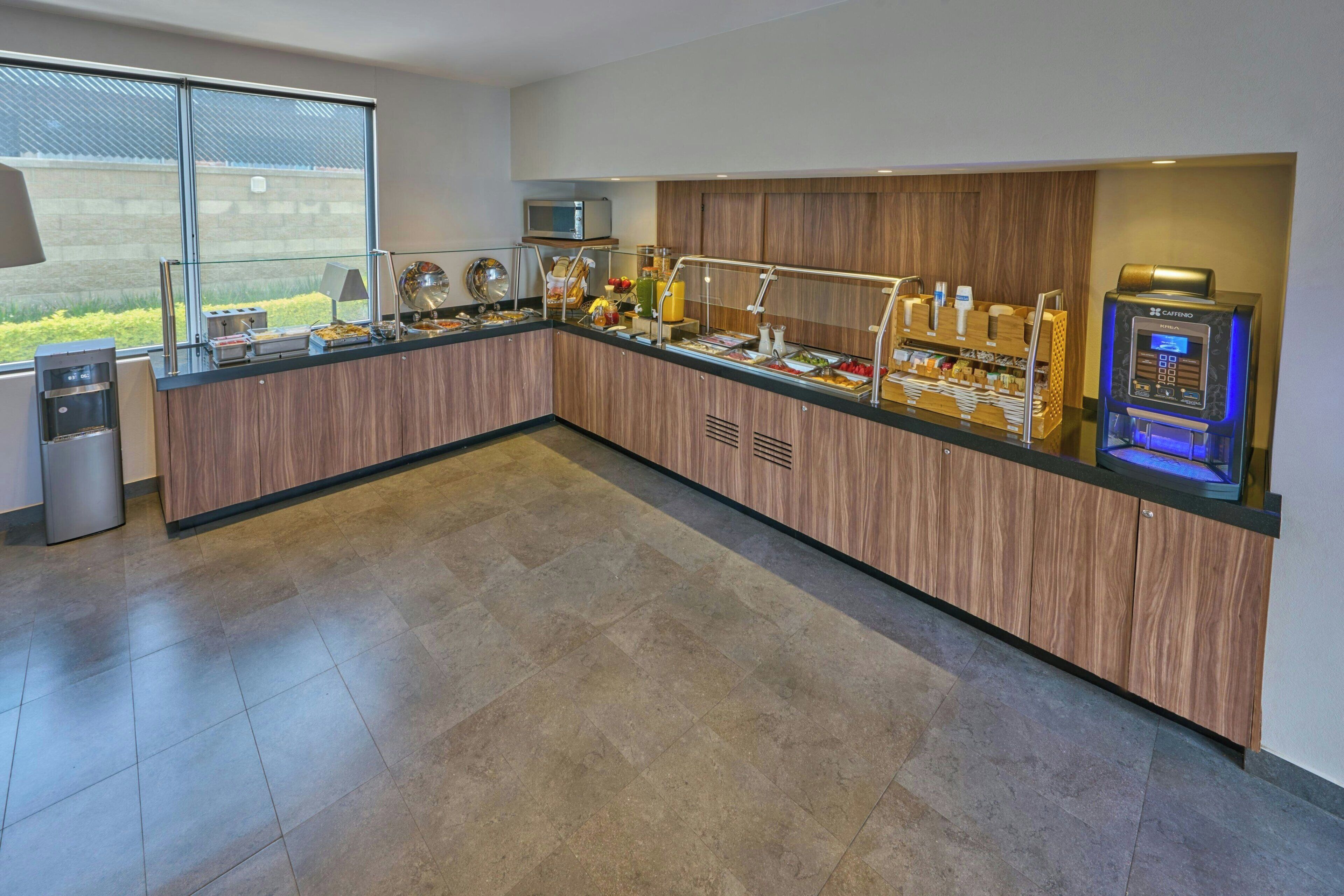 A modern breakfast bar with a microwave, coffee machine, and various food items.