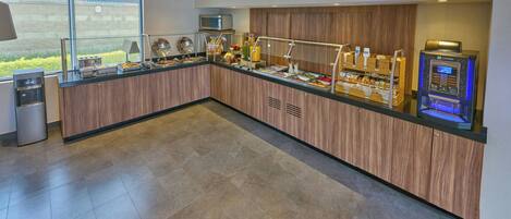 A modern breakfast bar with a microwave, coffee machine, and various food items.