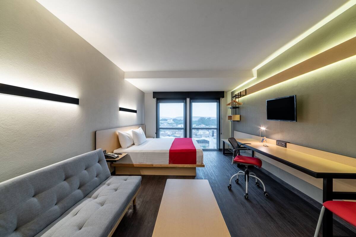 Habitació d'hotel moderna amb llit, sofà, escriptori i televisió.