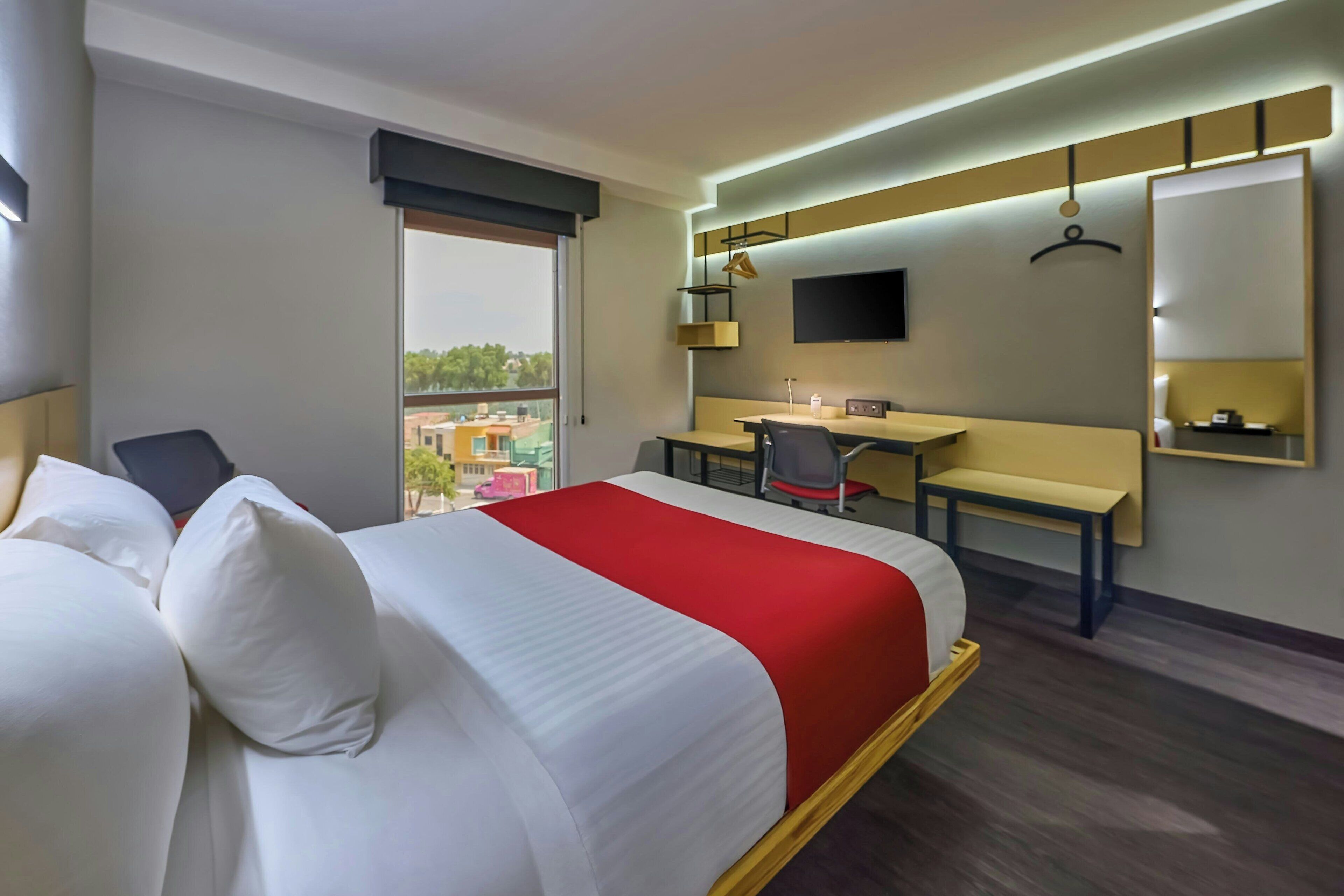 Una habitación de hotel con una cama, un escritorio, una silla, un televisor y una ventana.