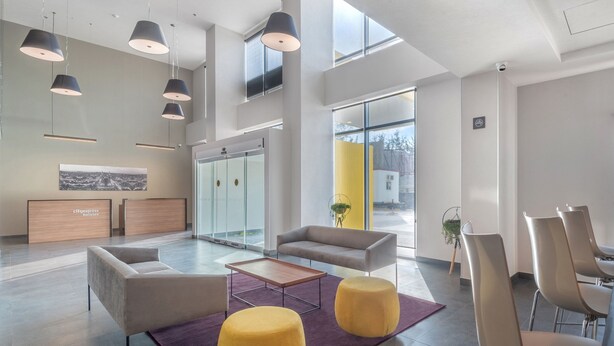 A modern lobby with seating, a reception desk, and a large window offering a city view.