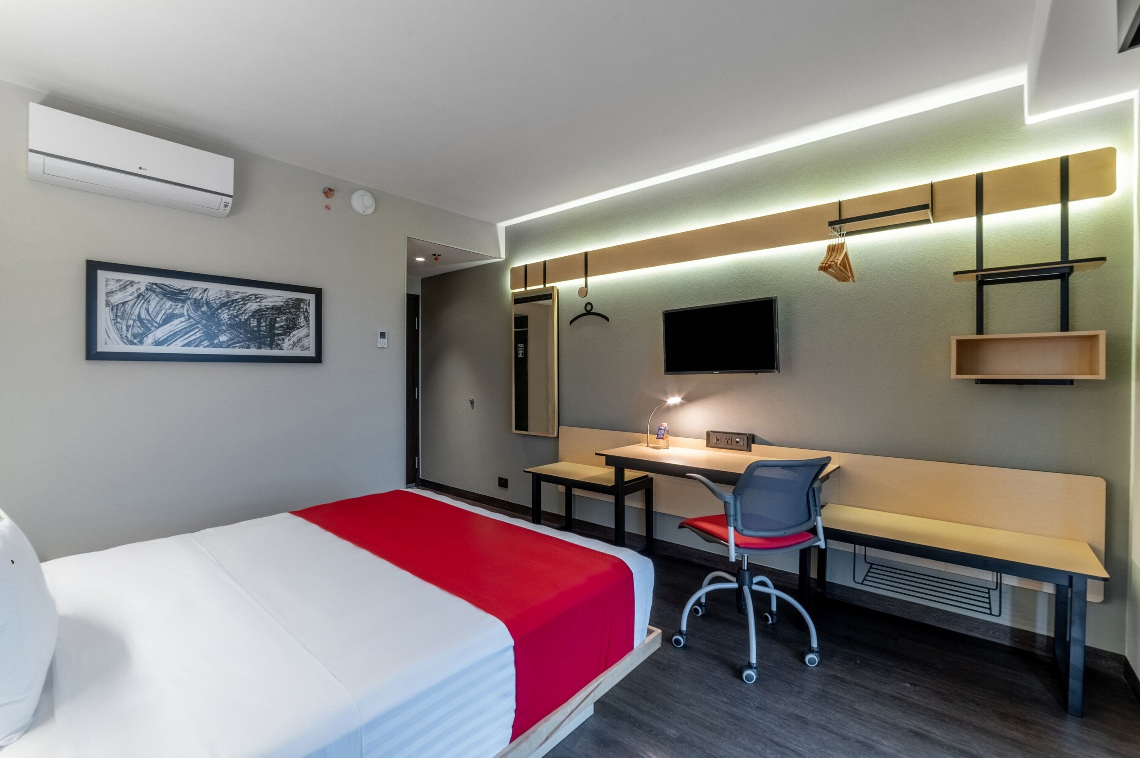 A hotel room with a bed, desk, chair, and a TV on the wall.