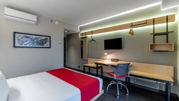A hotel room with a bed, desk, chair, and a TV on the wall.