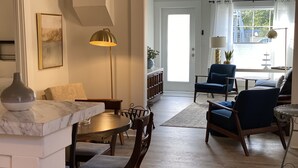Ein Wohnzimmer mit Essbereich, ausgestattet mit einer Marmorplatte, Holzsesseln, einem blauen Sofa und einem großen Fenster mit Vorhängen.
