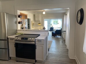 A modern kitchen with a built-in oven, a refrigerator, and a countertop. There is a dining area with a table and chairs visible through an open doorway. - Adorable cottage with modern style , we welcome you to your temporary home! (Sturgeon Bay)