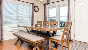 Un coin repas avec une table et des bancs en bois, une horloge au mur et une vue par la fenêtre.
