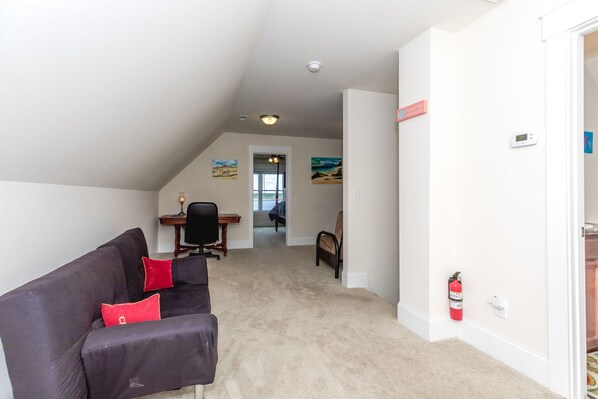 A room with a black couch, a desk, and a chair. There is a fire extinguisher on the wall.