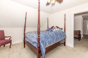 A four-poster bed with a patterned bedspread, a wooden chair, and a ceiling fan in a bedroom with beige carpet. - Out East Too - Soundfront Home with Amazing Views! Dog Friendly! (North Topsail Beach)