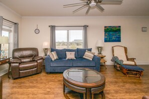A living room with a leather armchair, a blue sofa, a round coffee table, and a ceiling fan. - Out East Too - Soundfront Home with Amazing Views! Dog Friendly! (North Topsail Beach)
