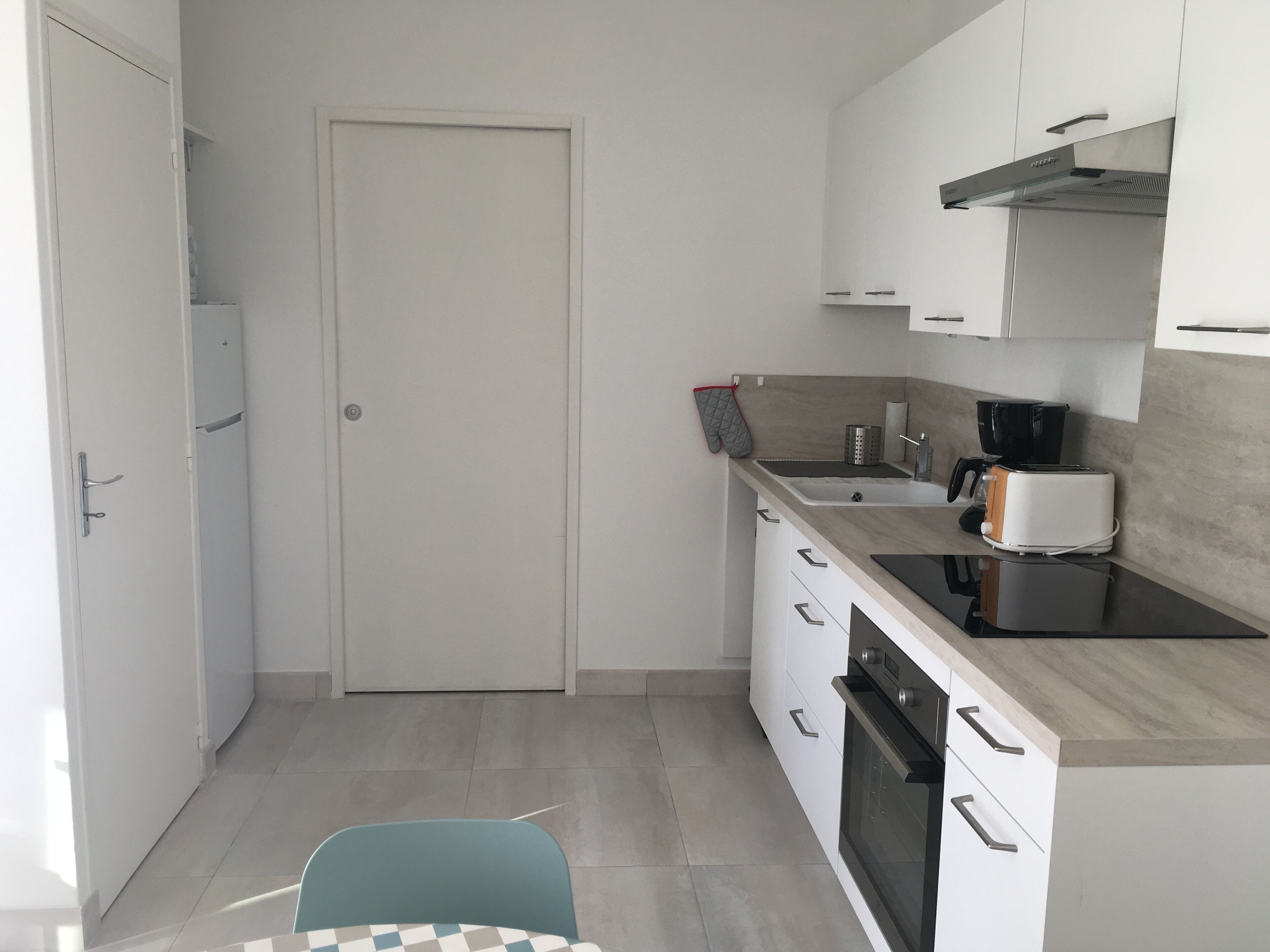 Une cuisine de taille réduite avec des meubles blancs, une cuisinière noire, une machine à café et un grille-pain.