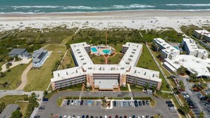 Luchtbeeld van een hotel met een centrale binnenplaats, meerdere gebouwen en een strand op de achtergrond.