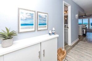Un couloir avec une console blanche, deux tableaux représentant des scènes de plage, une plante en pot et un panier en osier.