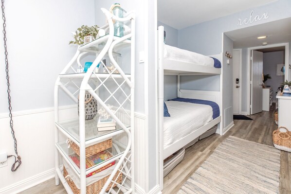 A bunk bed with a white metal ladder, a small shelf with decorative items, and a rug on the floor.