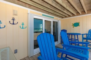 Un espace extérieur abrité, doté de chaises Adirondack bleues, d’une porte-fenêtre coulissante donnant sur une terrasse, et de décorations murales sur le thème de la marine.