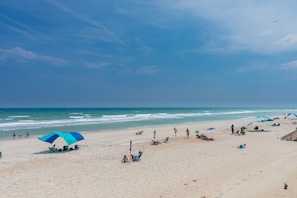 Une plage avec des parasols, des gens et l’océan.