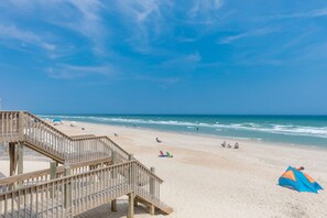 A beach with a wooden boardwalk leading to the shore, clear skies, and a few people enjoying the beach.