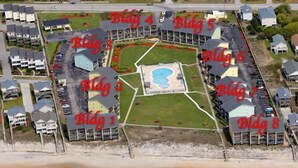 Ett flygfoton som visar ett hotellkomplex vid kusten, bestående av flera byggnader som är numrerade från byggnad 1 till byggnad 8. Bilden visar en central pool och direkt tillgång till stranden.