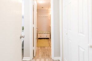 Un couloir mène à une chambre à coucher qui contient un lit, une table de chevet et un luminaire fixé au mur.