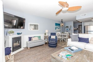 A living room with a fireplace, a ceiling fan, a dining area, and a kitchen. - Beachfront Bliss - Oceanfront 1 BR/1.5 BA at The Surf Condos! (Surf City)