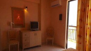 Quarto com cama, televisão sobre um móvel de madeira, duas cadeiras, uma mesinha e varanda com vista.