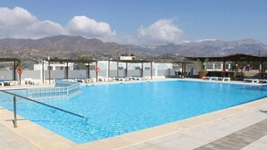Una piscina con agua cristalina azul, rodeada de sillas de descanso y sombrillas, con montañas al fondo.