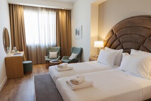 Une chambre d’hôtel avec un grand lit, deux chaises, un bureau avec une lampe et une vue sur l’extérieur par la fenêtre.