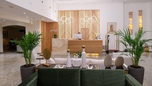 A modern reception area with a wooden partition, a reception desk, and a seating area with potted plants. - Patras Palace Hotel (Patras)