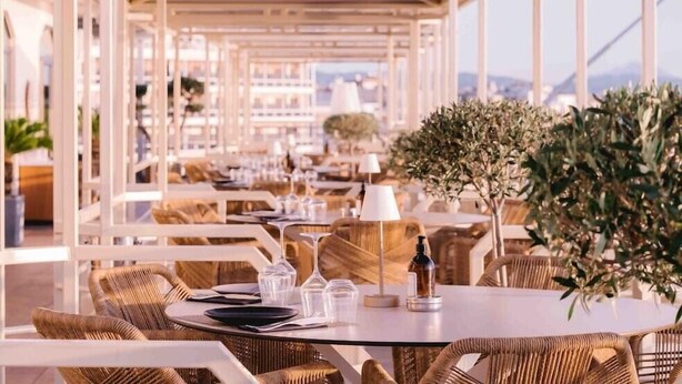 A rooftop restaurant with outdoor seating, white tables, wicker chairs, and a view of the cityscape. - Patras Palace Hotel (Patras)