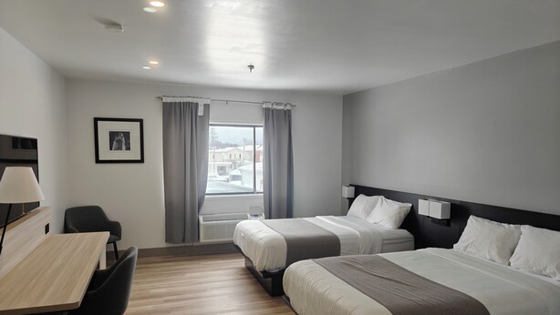 Habitación de hotel con dos camas, un escritorio con silla, un cuadro en la pared y una ventana con cortinas.