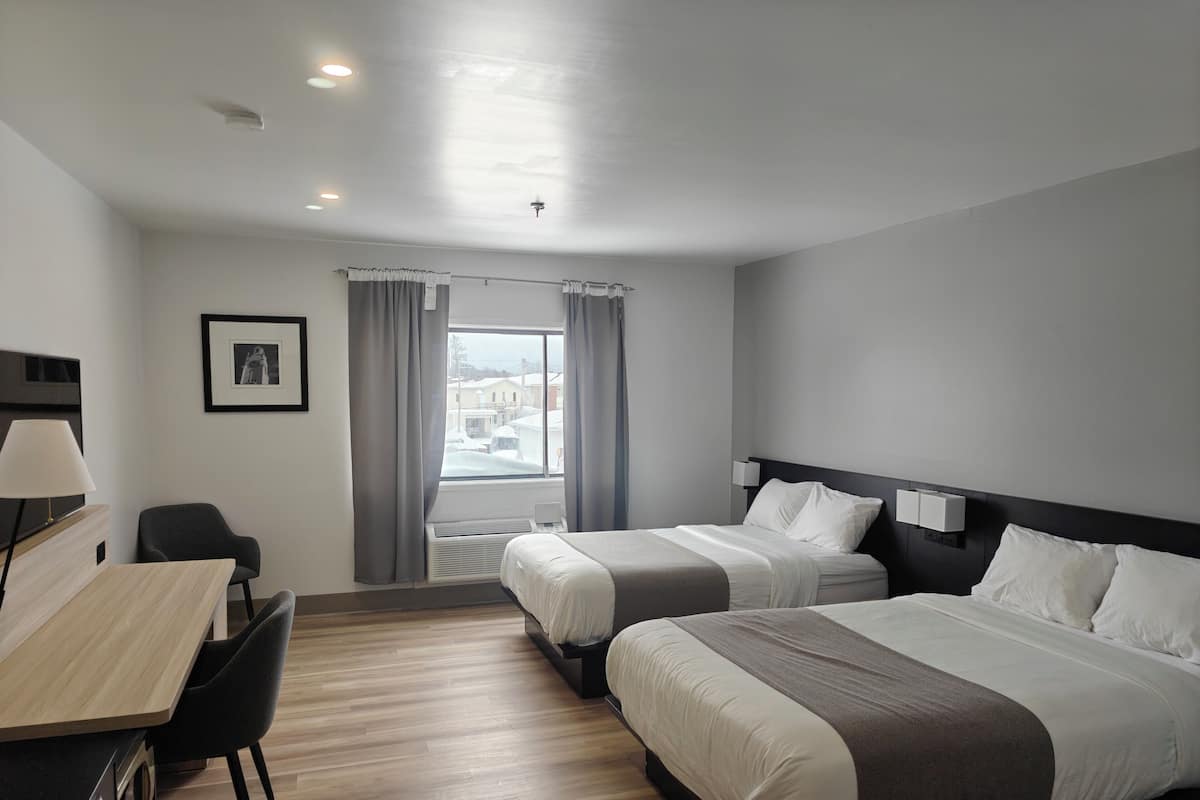 Habitación de hotel con dos camas, un escritorio con silla, un cuadro en la pared y una ventana con cortinas.