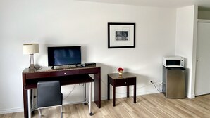 Habitación de hotel con escritorio, silla, televisor, cuadro enmarcado y microondas.