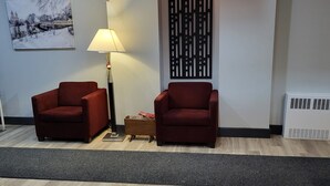Un vestíbulo con dos sillones rojos, una lámpara de pie, un panel decorativo y un cuadro en la pared.