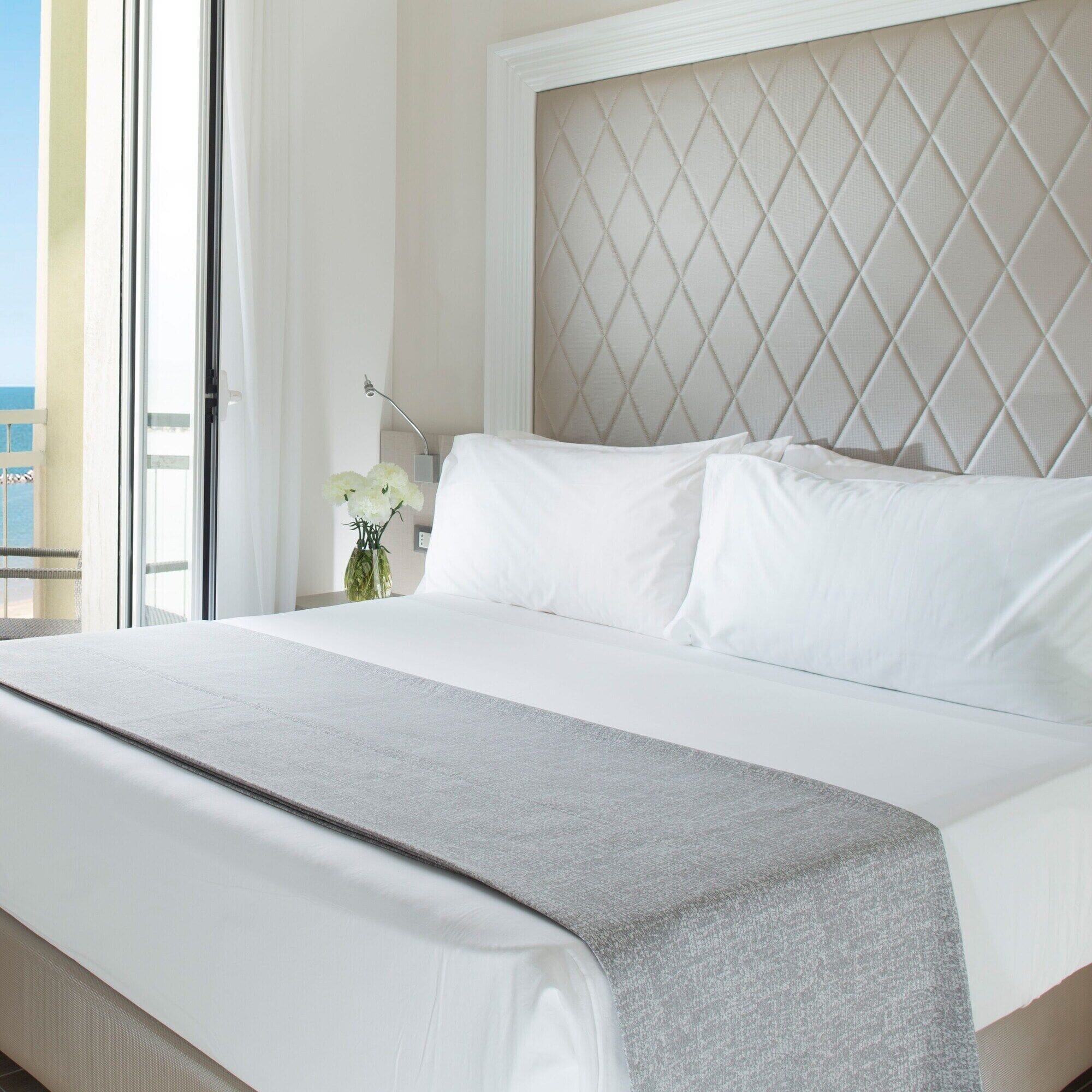 Quarto de hotel com uma cama grande, vista para o mar através de uma varanda e cabeceira decorativa.