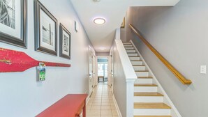 A hallway with a staircase, a red bench, and framed pictures on the wall.