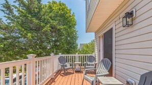 A wooden deck with a white railing, two Adirondack chairs, and a small table.