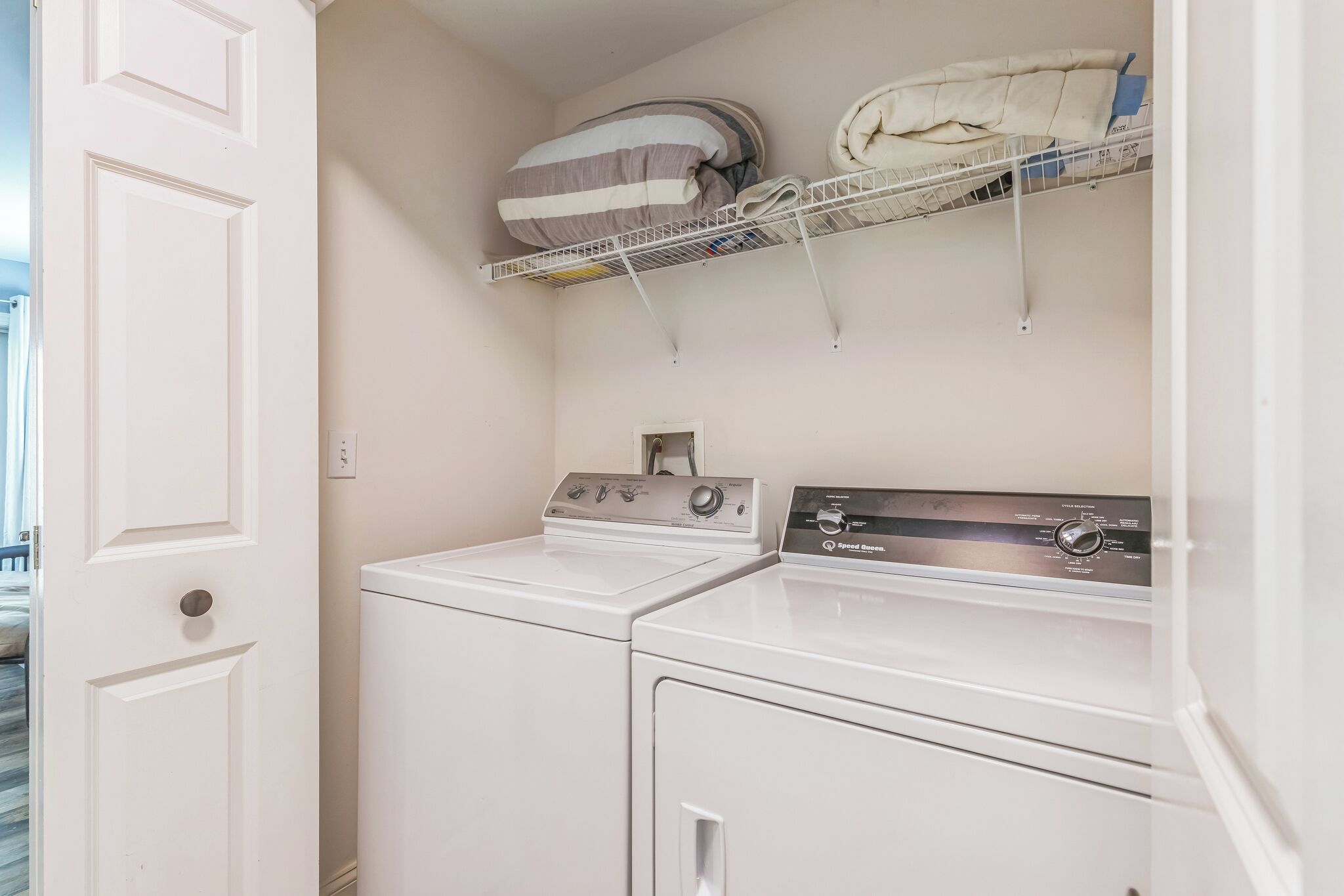 A laundry area with two white washing machines, a shelf with folded towels, and a white door.