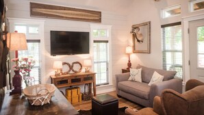 Ein gemütliches Wohnzimmer mit Fernseher, grauem Sofa und Couchtisch aus Holz.