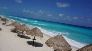 A beach with thatched umbrellas and a clear view of the turquoise ocean. - New Beachfront PH at Brisas By The Spot (Cancun)