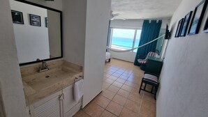 A bathroom with a sink, mirror, and towel rack. There is a bed with a view of the ocean in the background. - New Beachfront PH at Brisas By The Spot (Cancun)