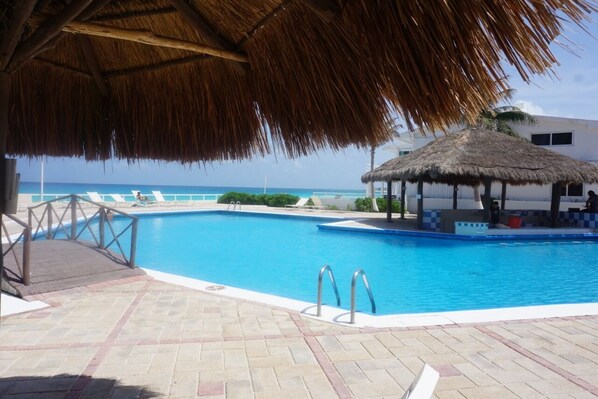 A swimming pool with a thatched roof structure, a lifeguard stand, and lounge chairs by the poolside.
